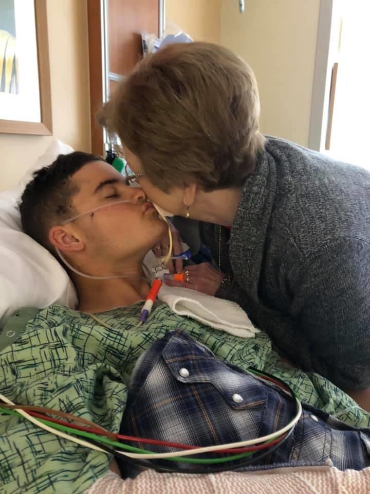 A grandmother kisses her Marine grandson as he lays in a hospital bed.