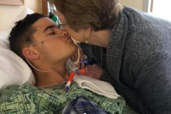 A grandmother kisses her Marine grandson as he lays in a hospital bed.