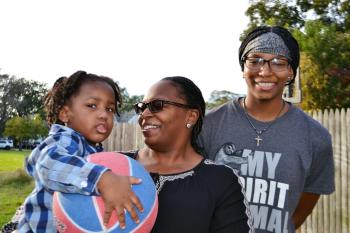 Mesha Clemons stands with her daughter and grandson in the backyard of her new home