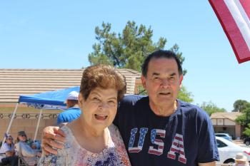 Alice and Robert, smiling while standing by the American Flag hanging on the front of their house.