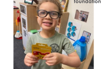 A young man in glasses hold up his prize of a gift card for completing all his homework!